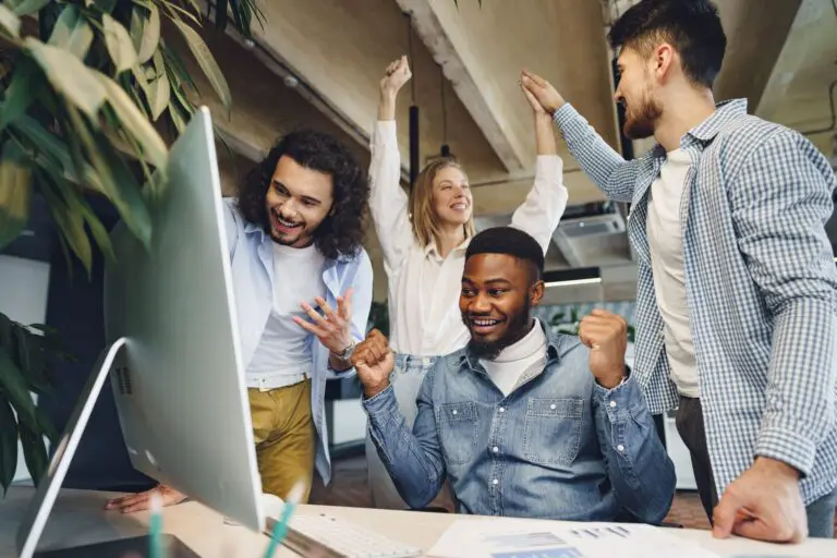 Quatro pessoas em frente ao computador comemorando