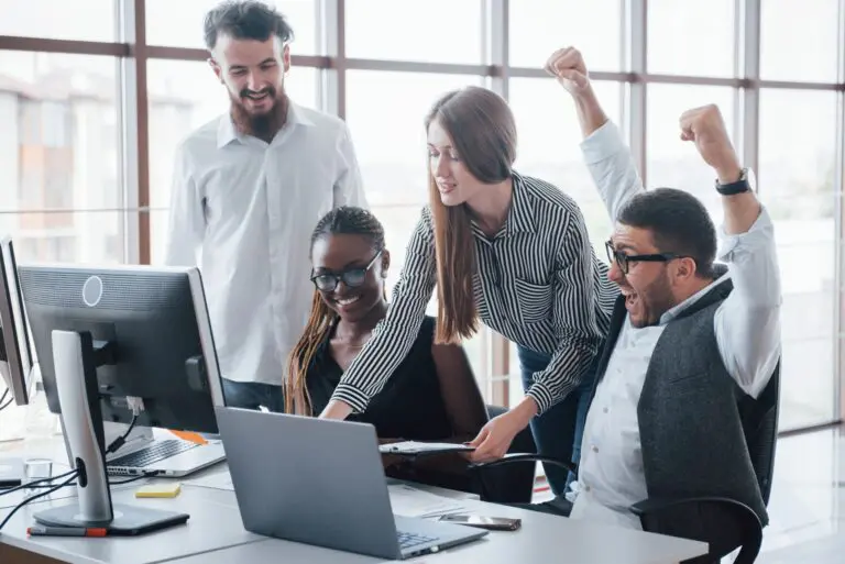 Quatro jovens colaboradores comemorando em frente ao computador